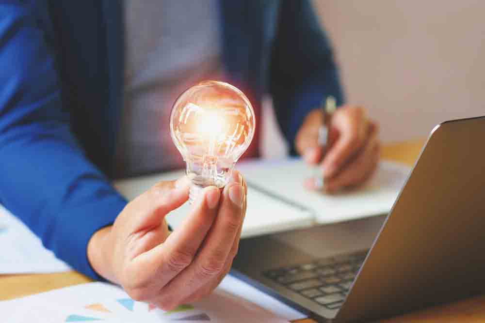 A man holding a lightbulb in front of a laptop